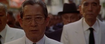 Movie still from “Year of the Dragon” (1985), directed by Michael Cimino – An older man wearing a suit and tie; Close Up shot, Over the shoulder angle