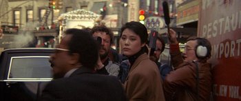 Movie still from “Year of the Dragon” (1985), directed by Michael Cimino – A group of people standing on the side of the street; Medium shot, Over the shoulder angle