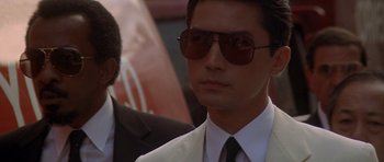 Movie still from “Year of the Dragon” (1985), directed by Michael Cimino – A man in a suit and sunglasses looking at the camera; Close Up shot, Over the shoulder angle