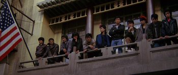 Movie still from “Year of the Dragon” (1985), directed by Michael Cimino – A group of young men sitting on top of a balcony; Wide shot, Low angle