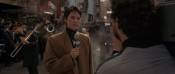 Movie still from “Year of the Dragon” (1985), directed by Michael Cimino – A woman is holding a microphone in front of a man; Medium shot, Over the shoulder angle