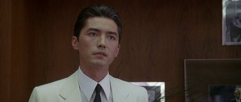 Movie still from “Year of the Dragon” (1985), directed by Michael Cimino – A man in a white suit and black tie; Close Up shot, Low angle