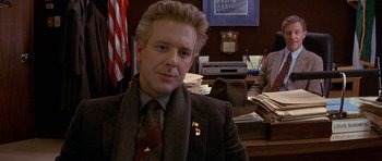 Movie still from “Year of the Dragon” (1985), directed by Michael Cimino – A man sitting in front of a desk in a room; Close Up shot, Over the shoulder angle