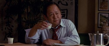 Movie still from “Year of the Dragon” (1985), directed by Michael Cimino – An asian man sitting at a table with a cup of coffee; Close Up shot, Low angle
