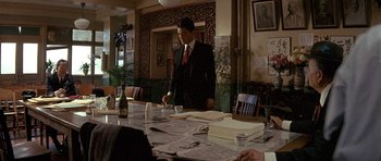 Movie still from “Year of the Dragon” (1985), directed by Michael Cimino – A man standing at a dining room table with papers; Medium shot, Over the shoulder angle