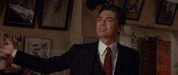 Movie still from “Year of the Dragon” (1985), directed by Michael Cimino – A man wearing a suit and tie in a room; Medium shot, Low angle