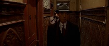 Movie still from “Year of the Dragon” (1985), directed by Michael Cimino – A man wearing a suit and a hat in a hallway; Close Up shot, Over the shoulder angle