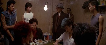Movie still from “Year of the Dragon” (1985), directed by Michael Cimino – A group of people sitting at a table eating food; Medium shot, Over the shoulder angle