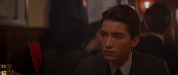 Movie still from “Year of the Dragon” (1985), directed by Michael Cimino – A person wearing a suit and tie; Close Up shot, Over the shoulder angle