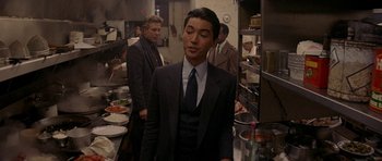 Movie still from “Year of the Dragon” (1985), directed by Michael Cimino – A man in a suit and tie standing in a kitchen; Medium shot, Over the shoulder angle