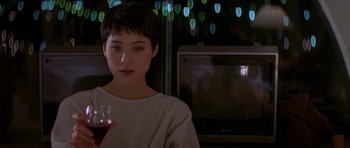 Movie still from “Year of the Dragon” (1985), directed by Michael Cimino – A woman sitting in front of a television holding a glass of red wine; Close Up shot, Over the shoulder angle
