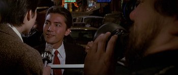 Movie still from “Year of the Dragon” (1985), directed by Michael Cimino – A man in a suit and tie taking a picture with his phone; Close Up shot, Over the shoulder angle