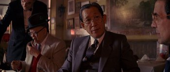 Movie still from “Year of the Dragon” (1985), directed by Michael Cimino – An older man wearing a suit and tie sitting in a chair; Close Up shot, Over the shoulder angle