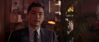 Movie still from “Year of the Dragon” (1985), directed by Michael Cimino – A person wearing a suit and tie; Close Up shot, Over the shoulder angle