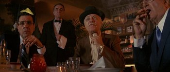 Movie still from “Year of the Dragon” (1985), directed by Michael Cimino – A man in a suit and a hat sitting at a table; Medium shot, Low angle
