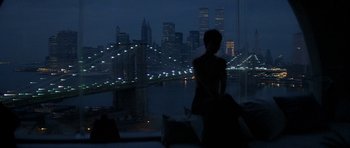 Movie still from “Year of the Dragon” (1985), directed by Michael Cimino – A woman standing on a ledge in front of a city skyline at night; Wide shot, Over the shoulder angle