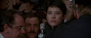 Movie still from “Year of the Dragon” (1985), directed by Michael Cimino – A man and a woman are standing in front of a microphone; Close Up shot, Over the shoulder angle