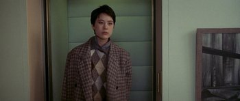Movie still from “Year of the Dragon” (1985), directed by Michael Cimino – A woman standing in front of a door wearing a suit and tie; Medium shot, Over the shoulder angle
