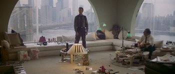 Movie still from “Year of the Dragon” (1985), directed by Michael Cimino – A man standing in a living room next to a lamp; Wide shot, High angle
