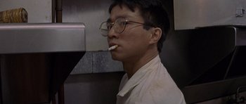 Movie still from “Year of the Dragon” (1985), directed by Michael Cimino – A man with glasses is smoking a cigarette; Close Up shot, Low angle