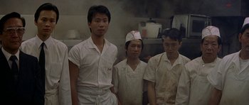 Movie still from “Year of the Dragon” (1985), directed by Michael Cimino – A group of men standing next to each other in a kitchen; Medium shot, High angle