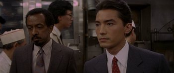 Movie still from “Year of the Dragon” (1985), directed by Michael Cimino – A man in a suit and tie standing next to another man; Close Up shot, High angle