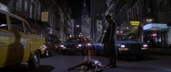 Movie still from “Year of the Dragon” (1985), directed by Michael Cimino – A woman laying on the ground in the middle of a street; Wide shot, Low angle