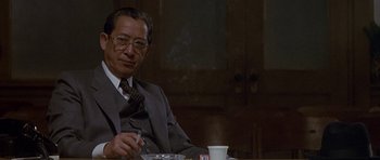 Movie still from “Year of the Dragon” (1985), directed by Michael Cimino – An older man sitting at a table with a cigarette in his mouth; Close Up shot, Low angle