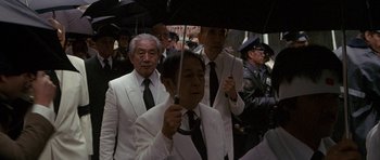Movie still from “Year of the Dragon” (1985), directed by Michael Cimino – A group of men in white suits and black ties holding black umbrellas; Medium shot, High angle