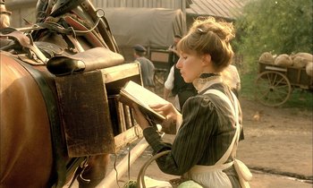 Movie still from “Yentl” (1983), directed by Barbra Streisand – A young woman is reading a book in front of an old wagon; Medium shot, High angle