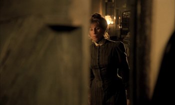 Movie still from “Yentl” (1983), directed by Barbra Streisand – A woman standing in a dimly - lit room; Medium shot, Over the shoulder angle