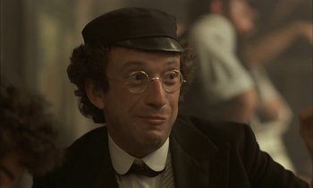 Movie still from “Yentl” (1983), directed by Barbra Streisand – A man in a hat and glasses wearing a suit; Close Up shot, Low angle