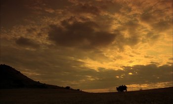Movie still from “Yentl” (1983), directed by Barbra Streisand – A truck is driving on a dirt road under a cloudy sky at sunset; Extreme Wide shot, Low angle