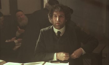 Movie still from “Yentl” (1983), directed by Barbra Streisand – A man in a suit and tie sitting at a table; Medium shot, Over the shoulder angle