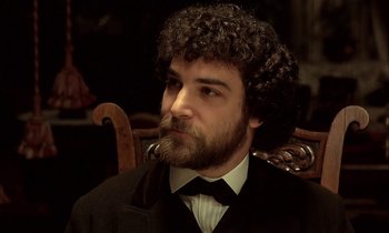 Movie still from “Yentl” (1983), directed by Barbra Streisand – A man with a beard and curly hair sitting in a chair; Close Up shot, High angle