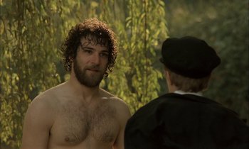 Movie still from “Yentl” (1983), directed by Barbra Streisand – A man with curly hair and a beard standing next to another man; Medium shot, Over the shoulder angle