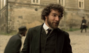 Movie still from “Yentl” (1983), directed by Barbra Streisand – A man in a suit and tie standing in front of a stone wall; Medium shot, Over the shoulder angle