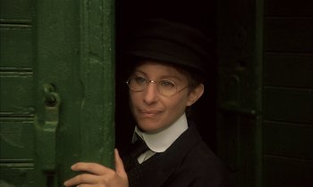 Movie still from “Yentl” (1983), directed by Barbra Streisand – A woman in a hat and glasses leaning against a green door; Close Up shot, High angle