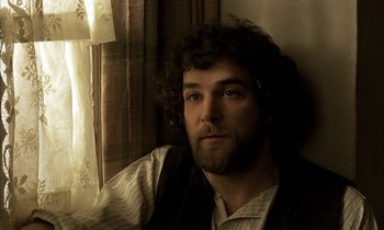 Movie still from “Yentl” (1983), directed by Barbra Streisand – A man with long hair and a beard sitting by a window; Close Up shot, High angle