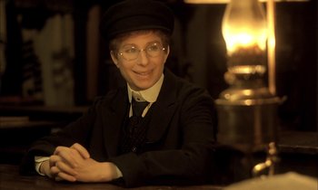 Movie still from “Yentl” (1983), directed by Barbra Streisand – A man in a suit and hat sitting at a table; Close Up shot, High angle