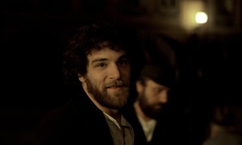 Movie still from “Yentl” (1983), directed by Barbra Streisand – A man with a goatee and a beard is smiling for the camera; Close Up shot, Over the shoulder angle