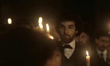 Movie still from “Yentl” (1983), directed by Barbra Streisand – A group of people standing in the dark holding lit candles; Medium shot, Over the shoulder angle