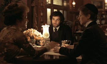 Movie still from “Yentl” (1983), directed by Barbra Streisand – A man sitting at a table with two other people; Medium shot, Over the shoulder angle