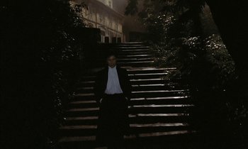 Movie still from “Yentl” (1983), directed by Barbra Streisand – A man in a suit standing in front of some stairs; Wide shot, High angle