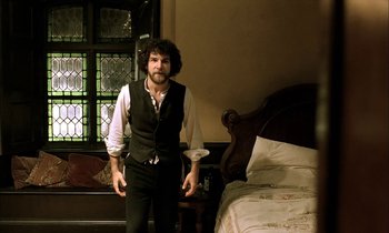 Movie still from “Yentl” (1983), directed by Barbra Streisand – A man standing in front of a bed in a room; Medium shot, Low angle