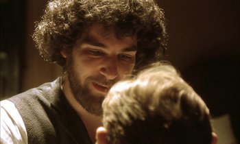 Movie still from “Yentl” (1983), directed by Barbra Streisand – A man with curly hair is looking at the camera; Close Up shot, Over the shoulder angle