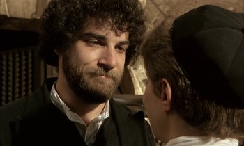 Movie still from “Yentl” (1983), directed by Barbra Streisand – A man with curly hair and beard talking to another man; Close Up shot, Over the shoulder angle