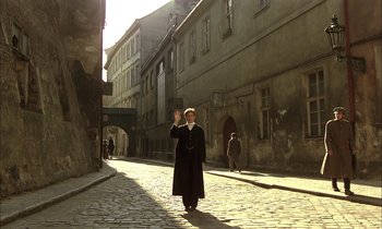 Movie still from “Yentl” (1983), directed by Barbra Streisand – A man in a long black coat standing on a brick street; Wide shot, High angle