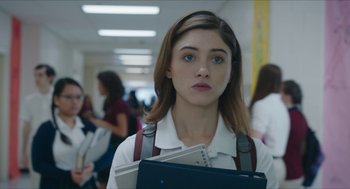 Movie still from “Yes, God, Yes” (2019), directed by Karen Maine – A girl in a white shirt is holding some papers; Close Up shot, Over the shoulder angle