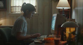 Movie still from “Yes, God, Yes” (2019), directed by Karen Maine – A woman sitting at a table using a computer; Medium shot, High angle